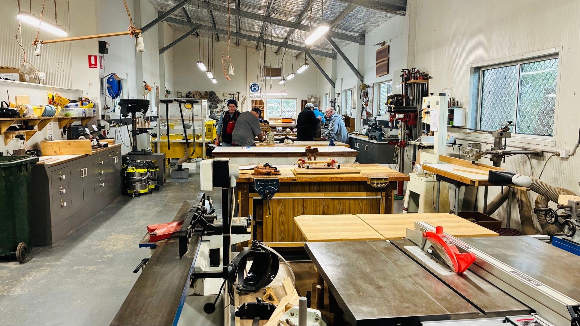 Woodworking studio with tools, equipment, and people working at benches.