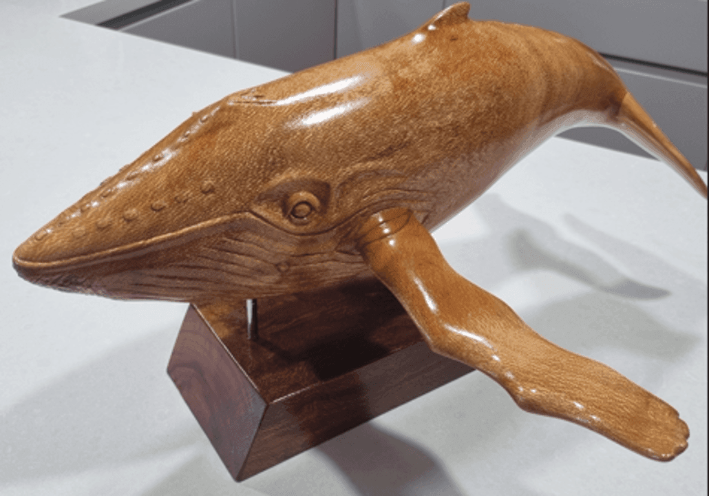 Wooden whale sculpture on a pedestal, depicting a detailed and textured marine animal in brown color.