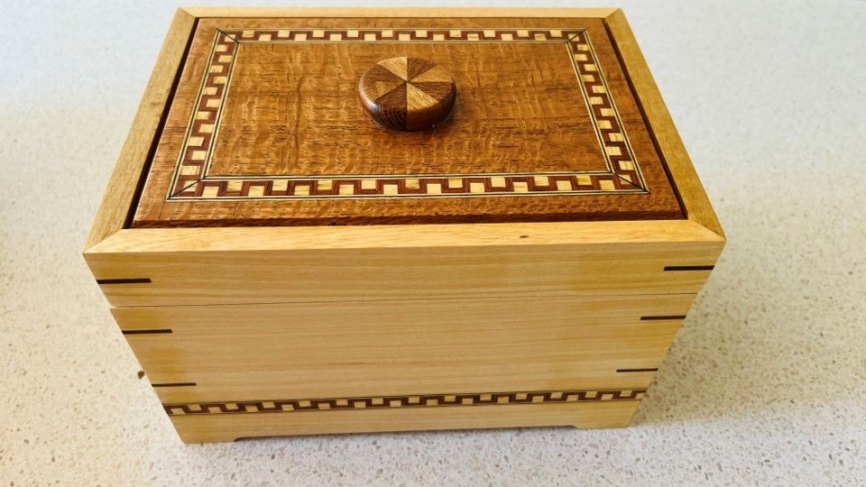 Decorative wooden box with intricate inlay patterns and a circular knob on the lid.