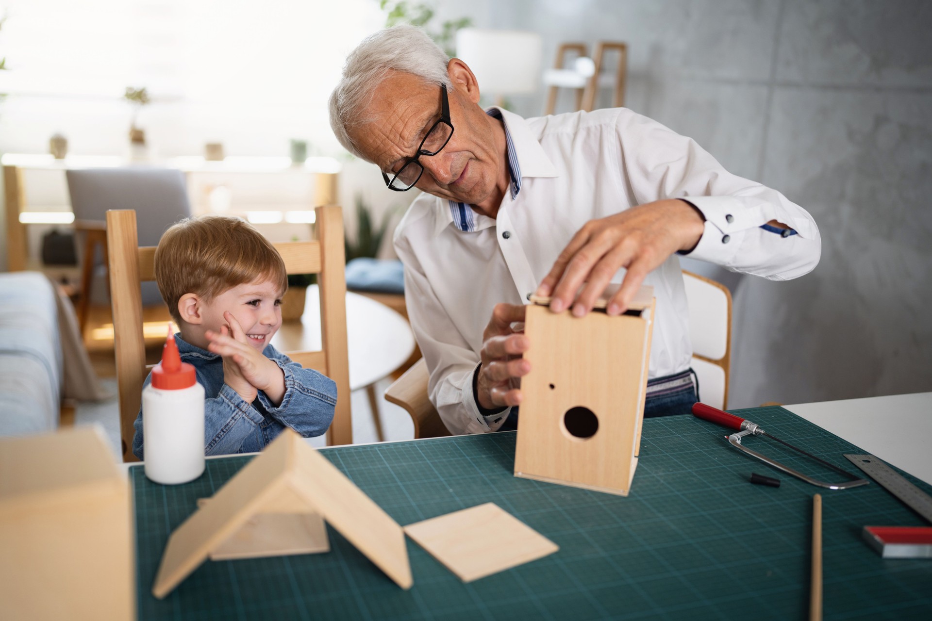 Excited toddler boy applauding while his grandfather making the birdhouse